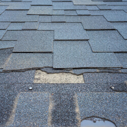 Close Up View Of Bitumen Shingles Roof Damage That Needs Repair.